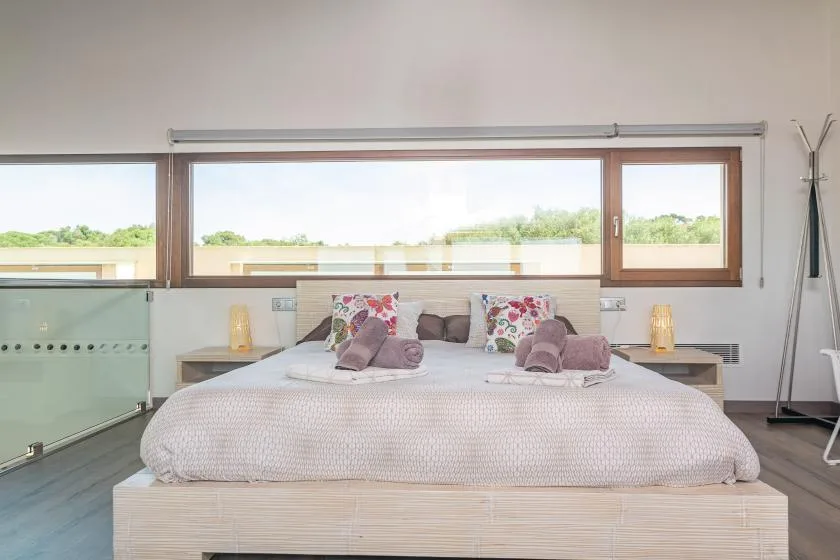 A bright bedroom features a bed beneath a wide window overlooking greenery.