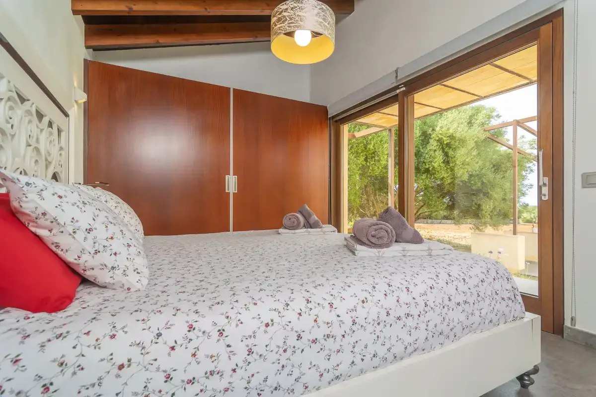 A bedroom with a floral bedspread beside open sliding glass doors.