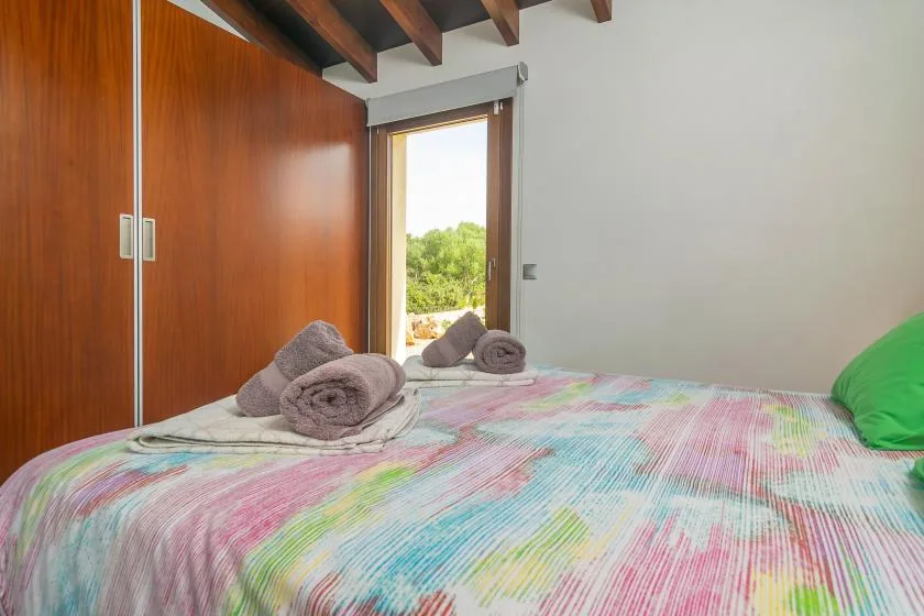 A bedroom with a colorful bedspread and a window overlooking greenery.