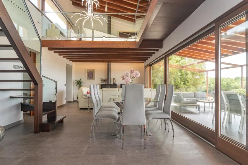 A dining area with a long table and chairs sits beside large glass doors.
