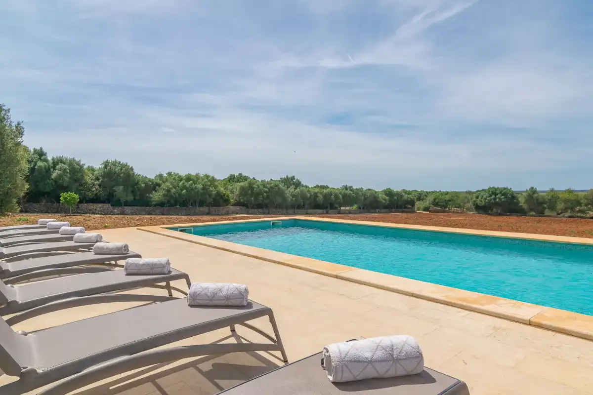 An outdoor swimming pool is surrounded by a sunny deck with lounge seating.