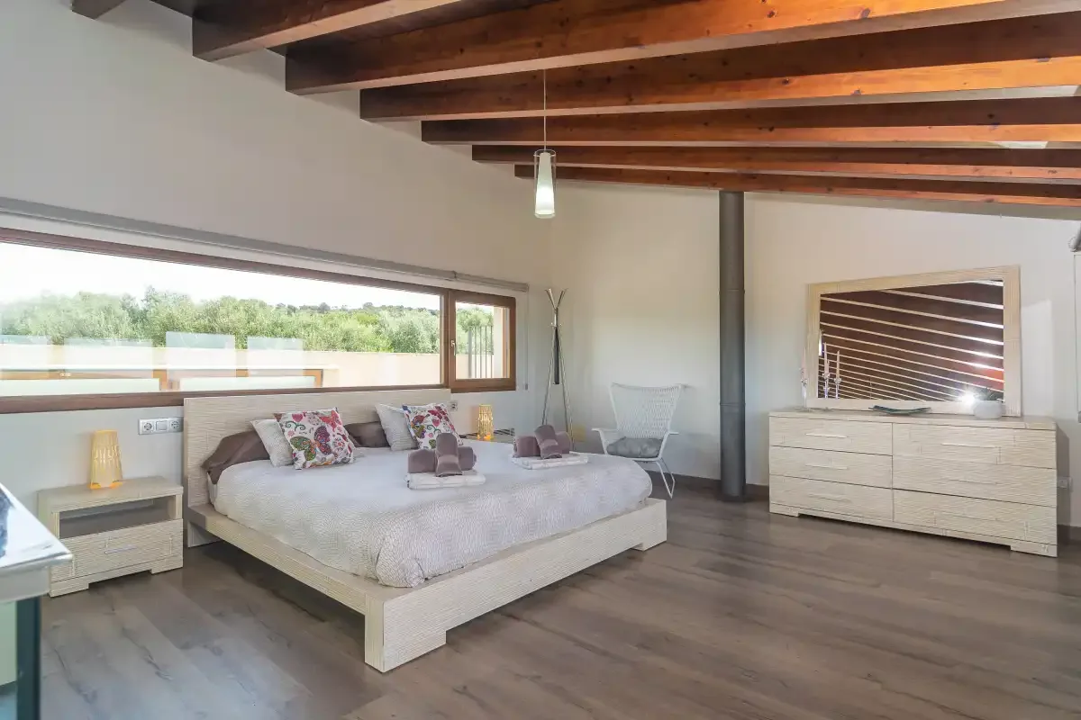 A bedroom with a large bed beneath exposed wooden ceiling beams.
