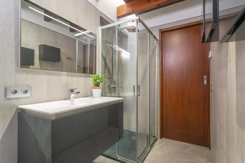 A modern bathroom with a glass shower, vanity, and wooden door.