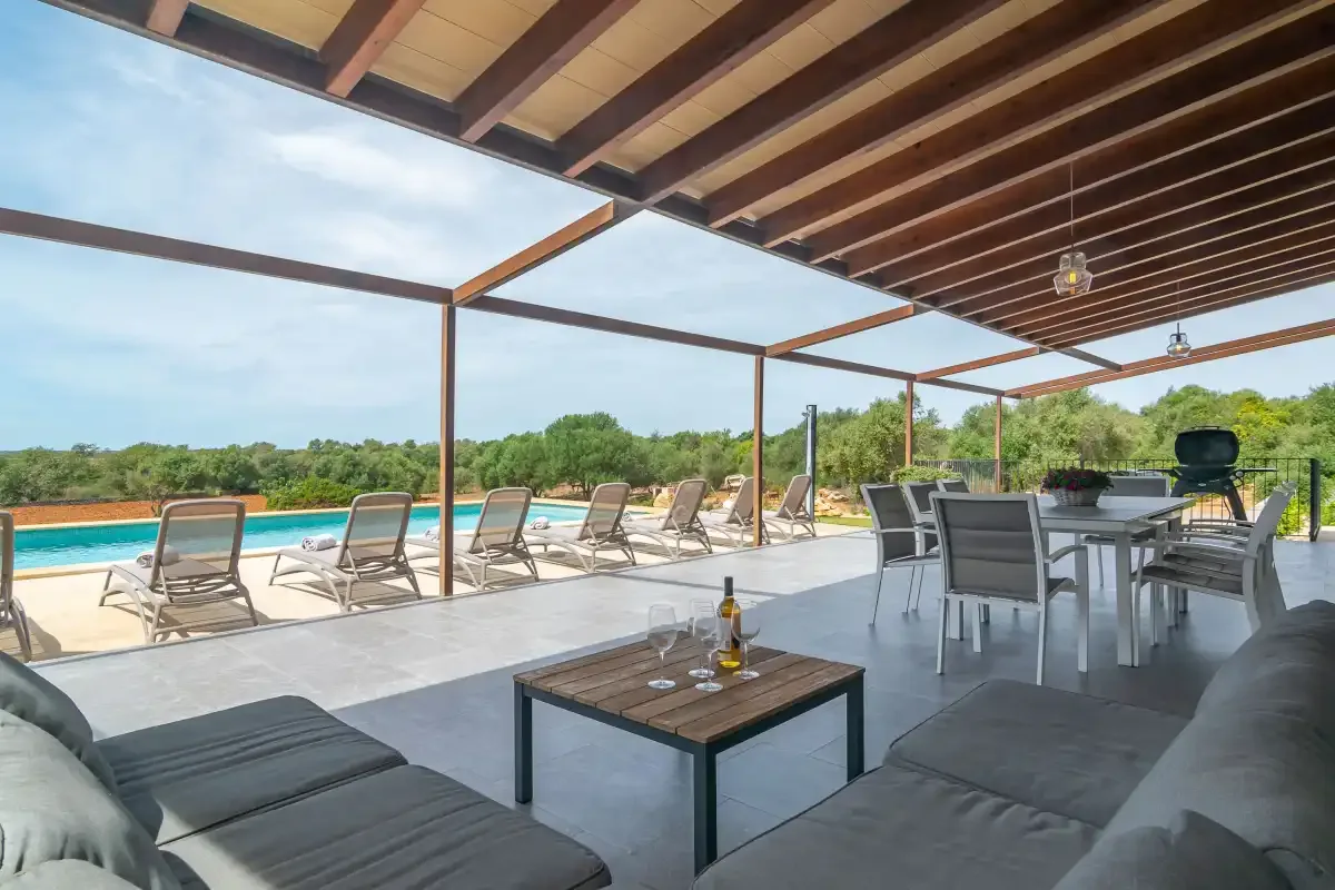 A covered outdoor patio has lounge seating, a dining table, and a swimming pool nearby.
