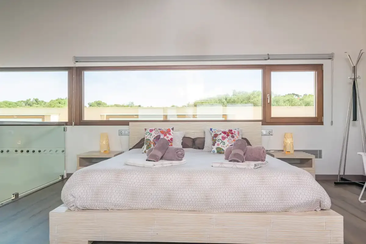 A bright bedroom with a large bed positioned beneath wide windows.