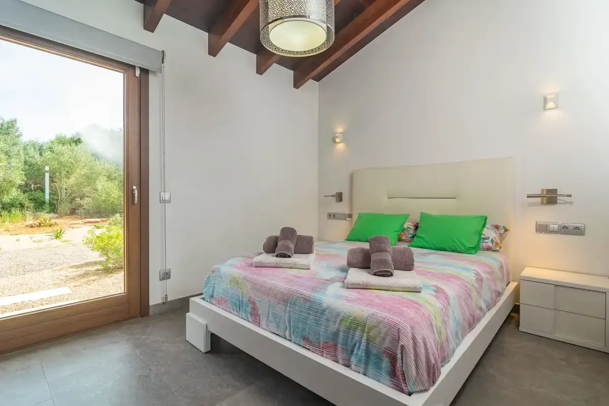 A bedroom with a bed dressed in colorful bedding beside a large glass door.