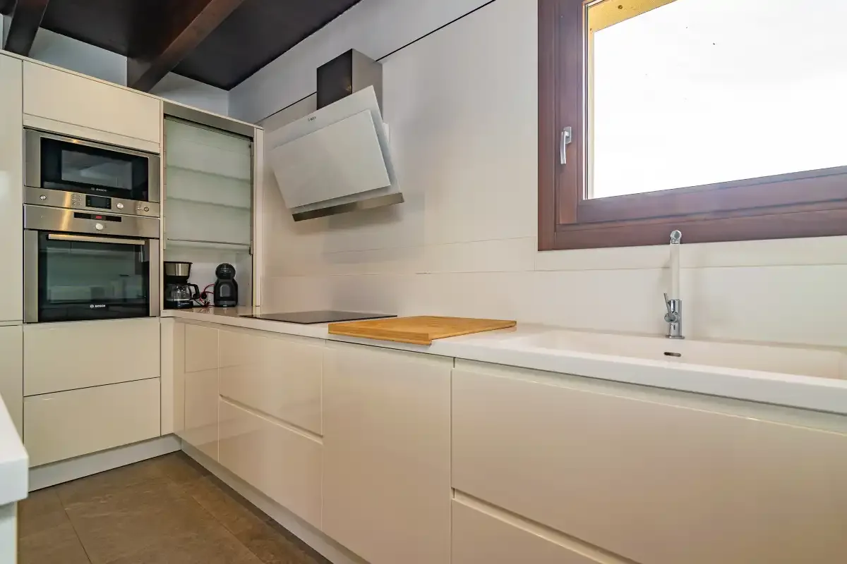 A modern kitchen with built-in appliances and a long countertop beneath a window.