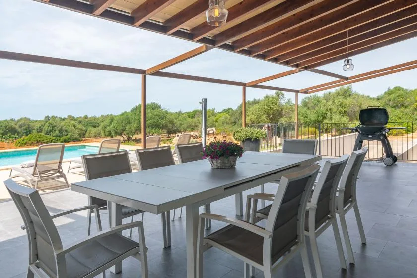 A covered outdoor dining area with a long table overlooking a swimming pool.