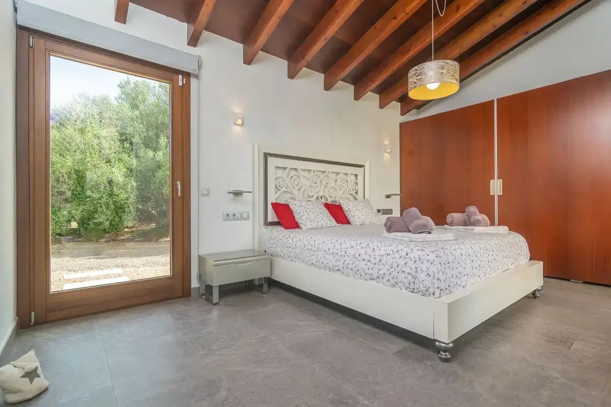 A bedroom with a large bed beside a glass door opening onto greenery.