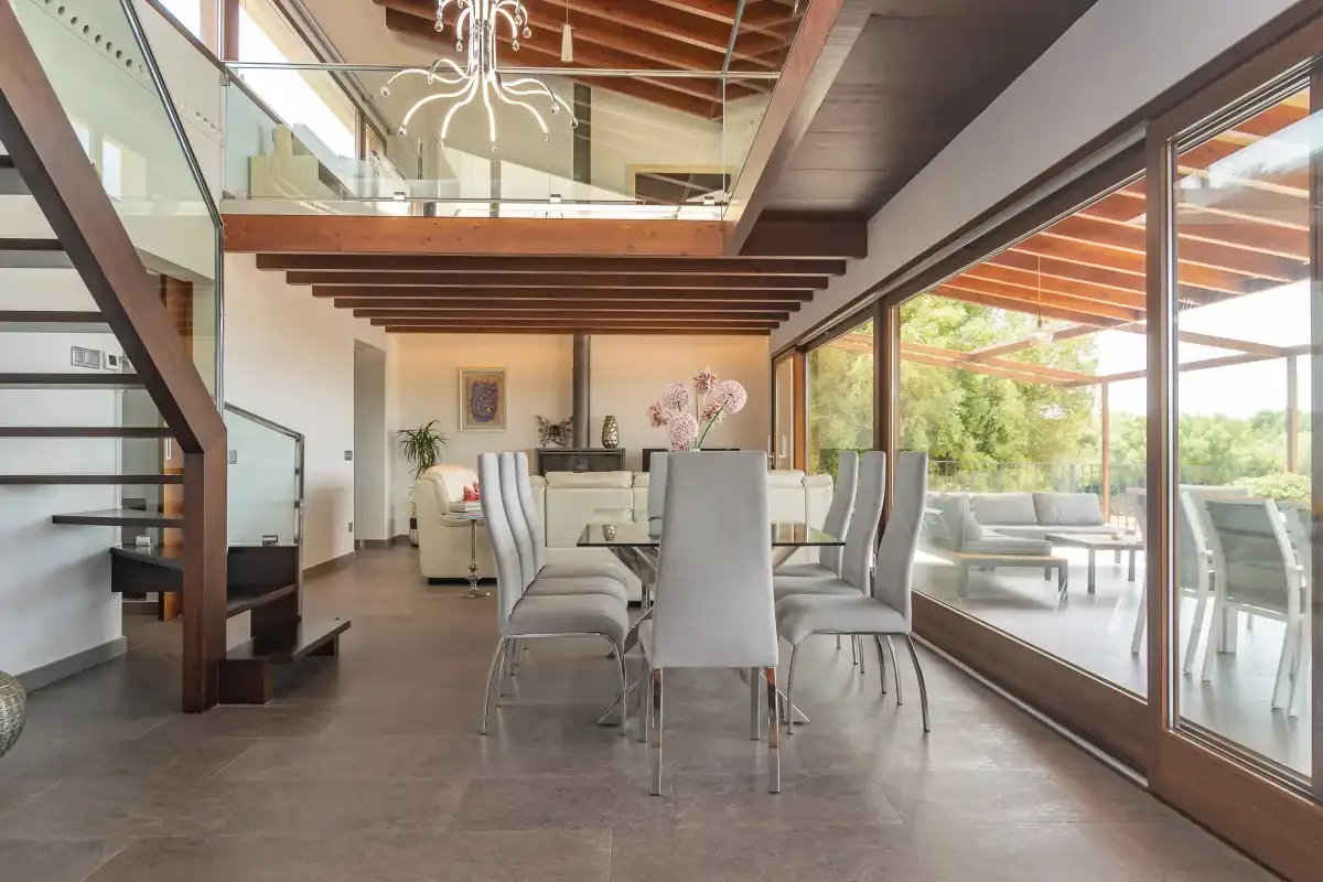 A dining area with a long table and chairs beside large glass doors.
