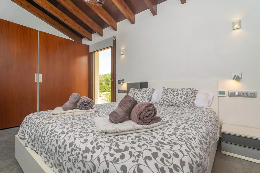 A bedroom with a large bed covered in patterned bedding and wooden ceiling beams.