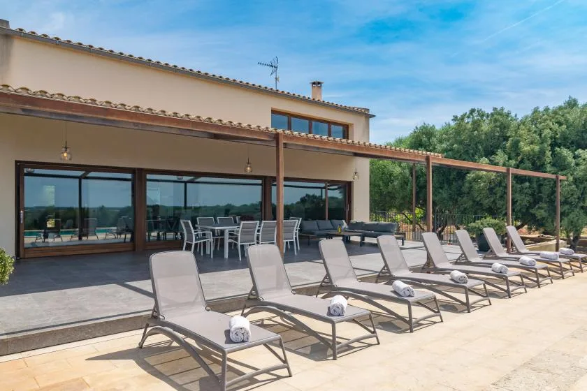 A poolside patio with lounge seating beside a house and glass doors.