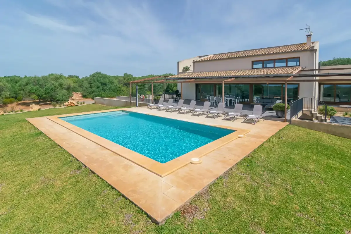 A modern house overlooks a swimming pool and surrounding lawn.