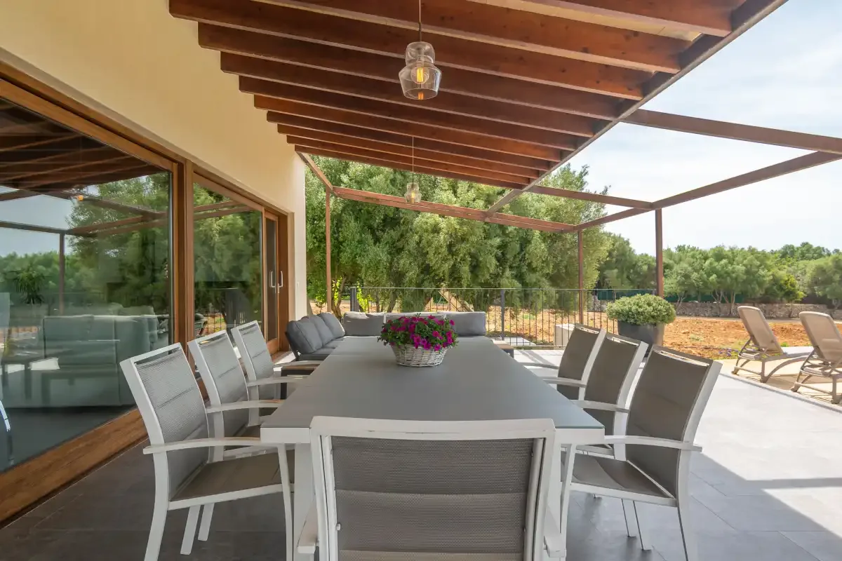 A covered outdoor dining area with a long table and garden views.