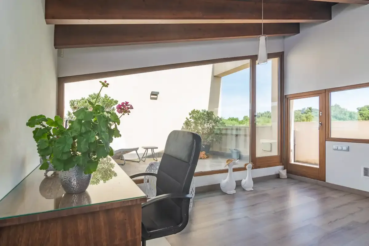 A bright room with a desk, office chair, and large windows overlooking greenery.