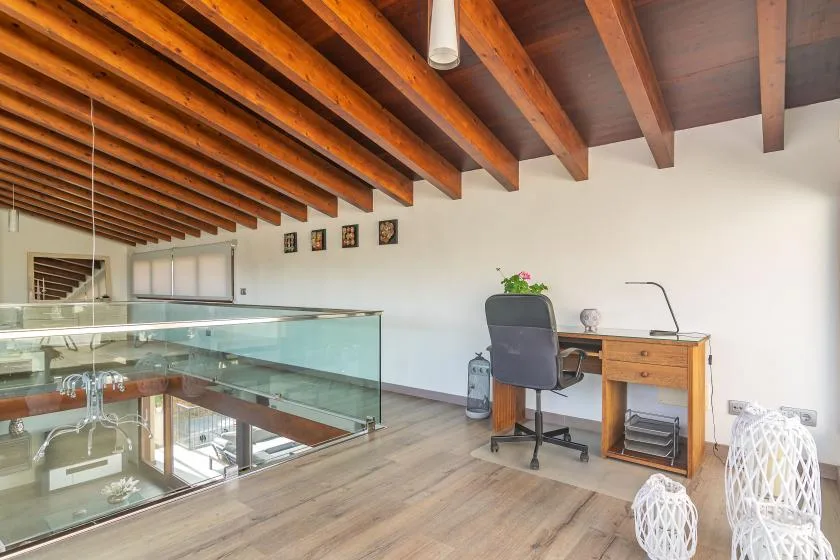 A bright loft workspace with a desk beneath exposed wooden ceiling beams.