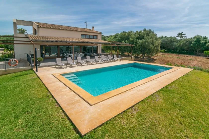A swimming pool beside a modern house, with lounge seating on the patio.