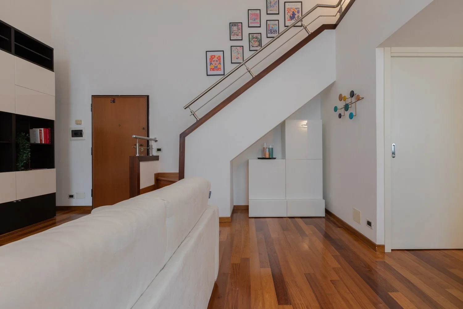 Una luminosa sala de estar con sofá blanco, suelo de madera y una escalera.