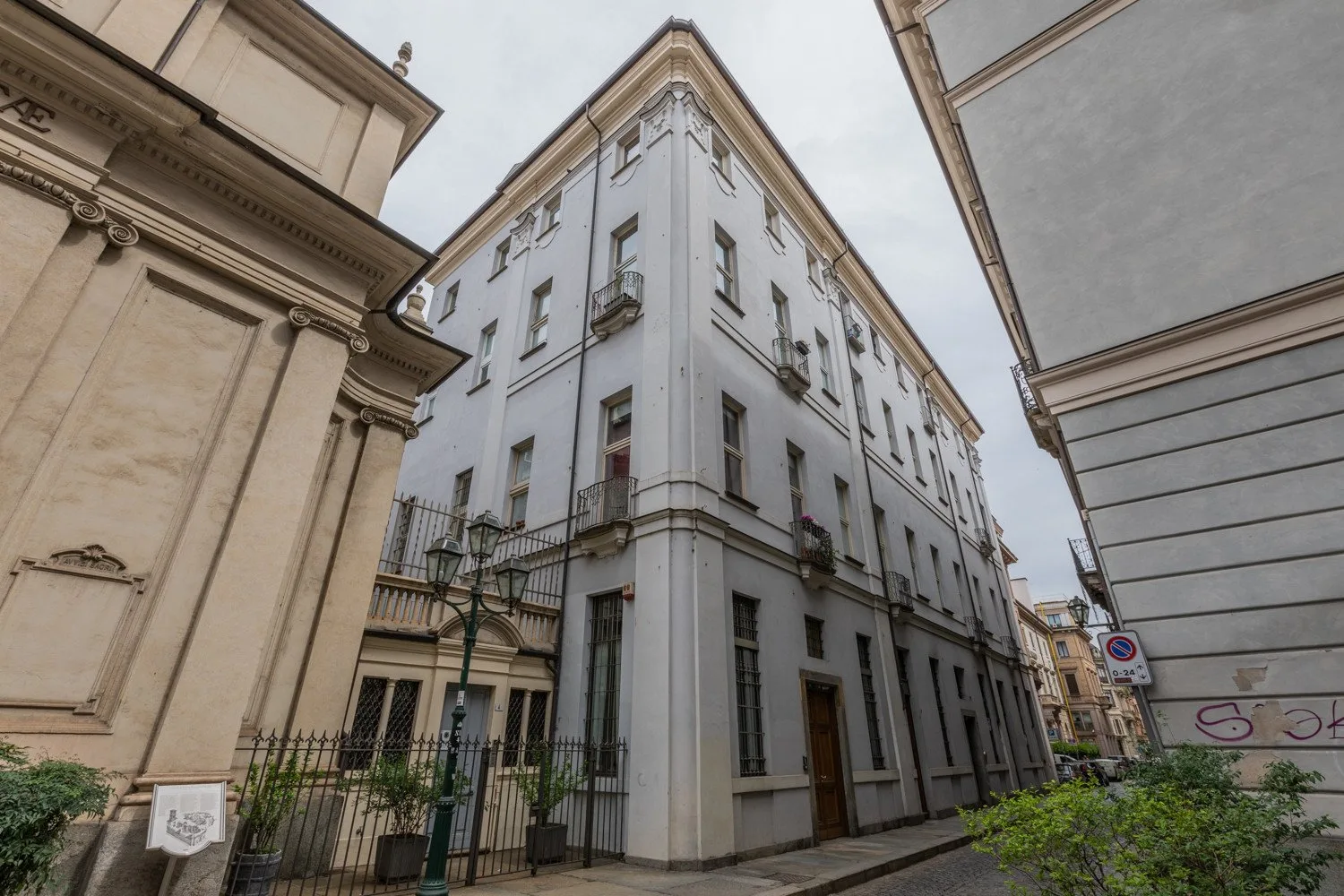 Una calle estrecha flanqueada por edificios altos, con un edificio claro en una esquina.