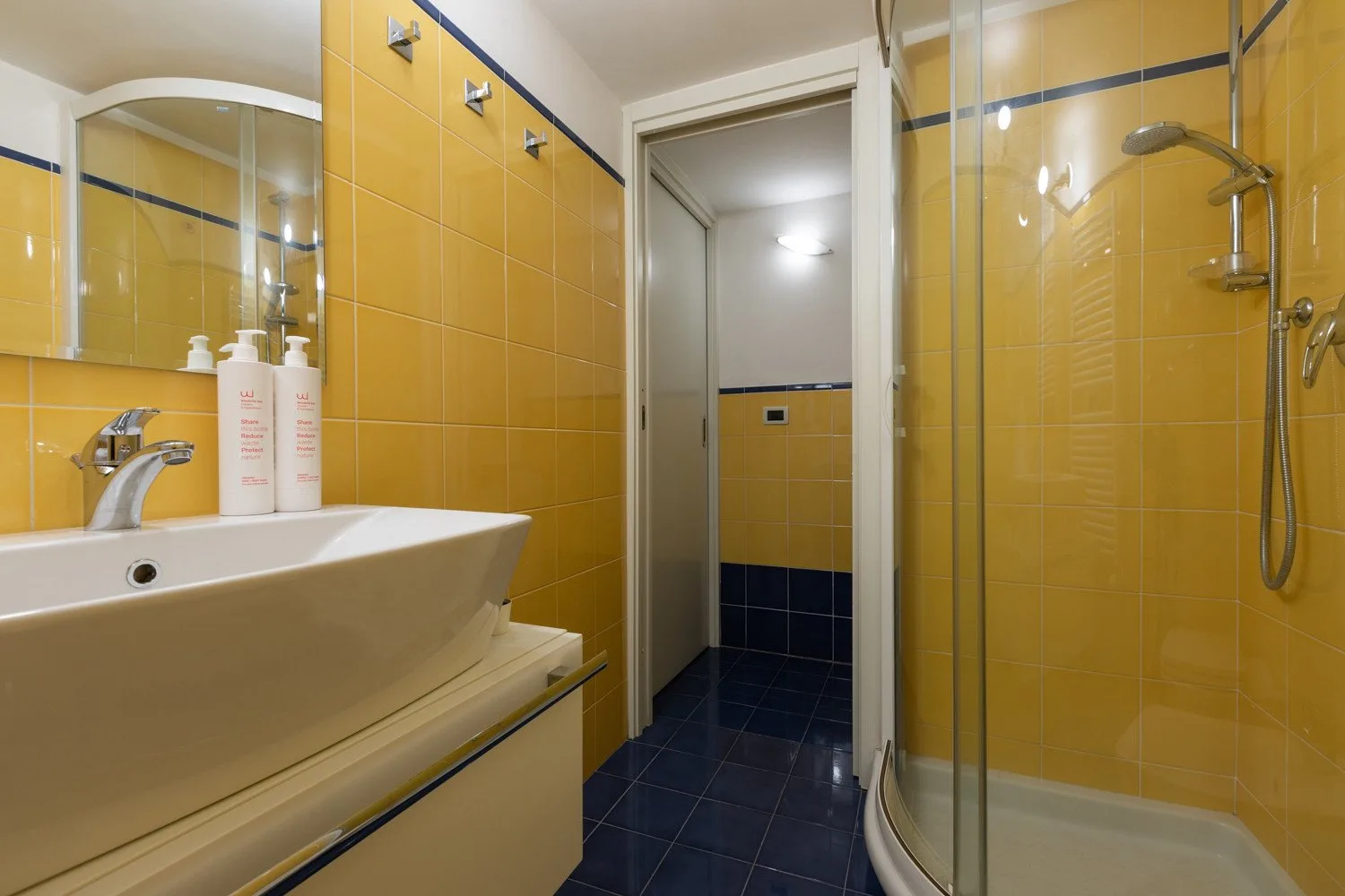 Un baño alicatado con lavabo y ducha con mampara de vidrio.