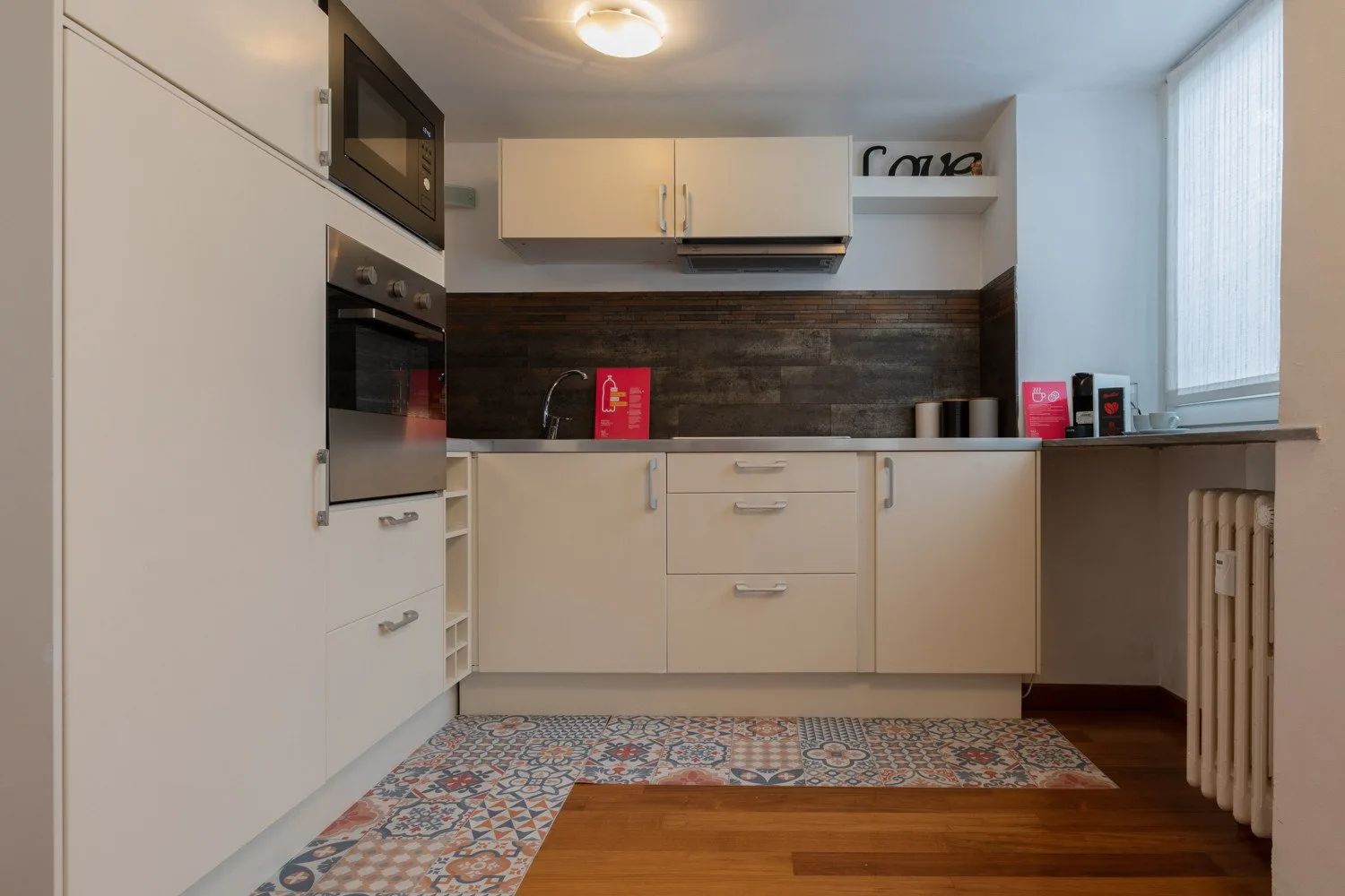 Una cocina compacta con armarios claros, un salpicadero oscuro y baldosas estampadas.