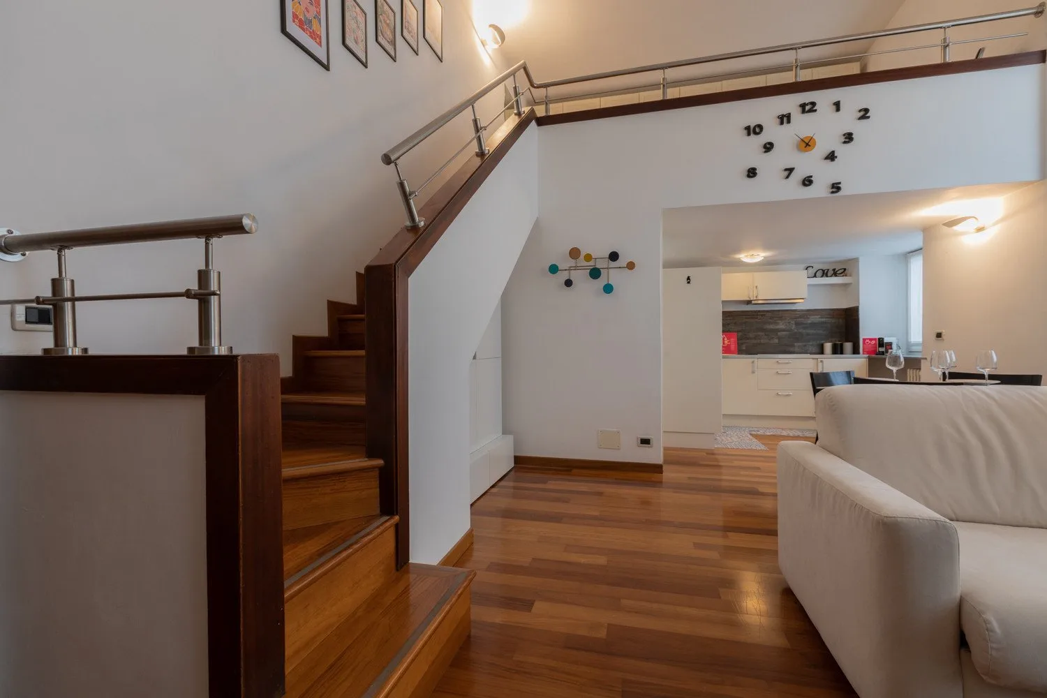 Una sala luminosa con una escalera de madera y una cocina abierta.