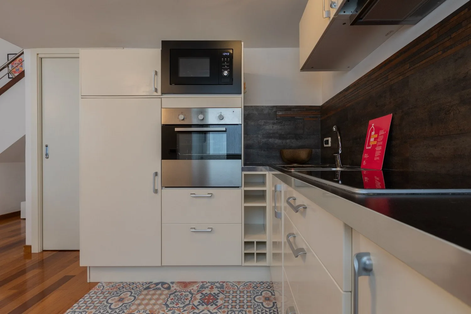 Una cocina moderna con gabinetes blancos, electrodomésticos empotrados y una encimera oscura.