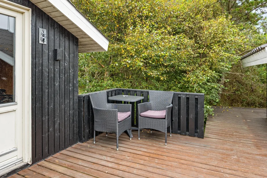 An outdoor deck has a small seating area beside a dark wooden building.