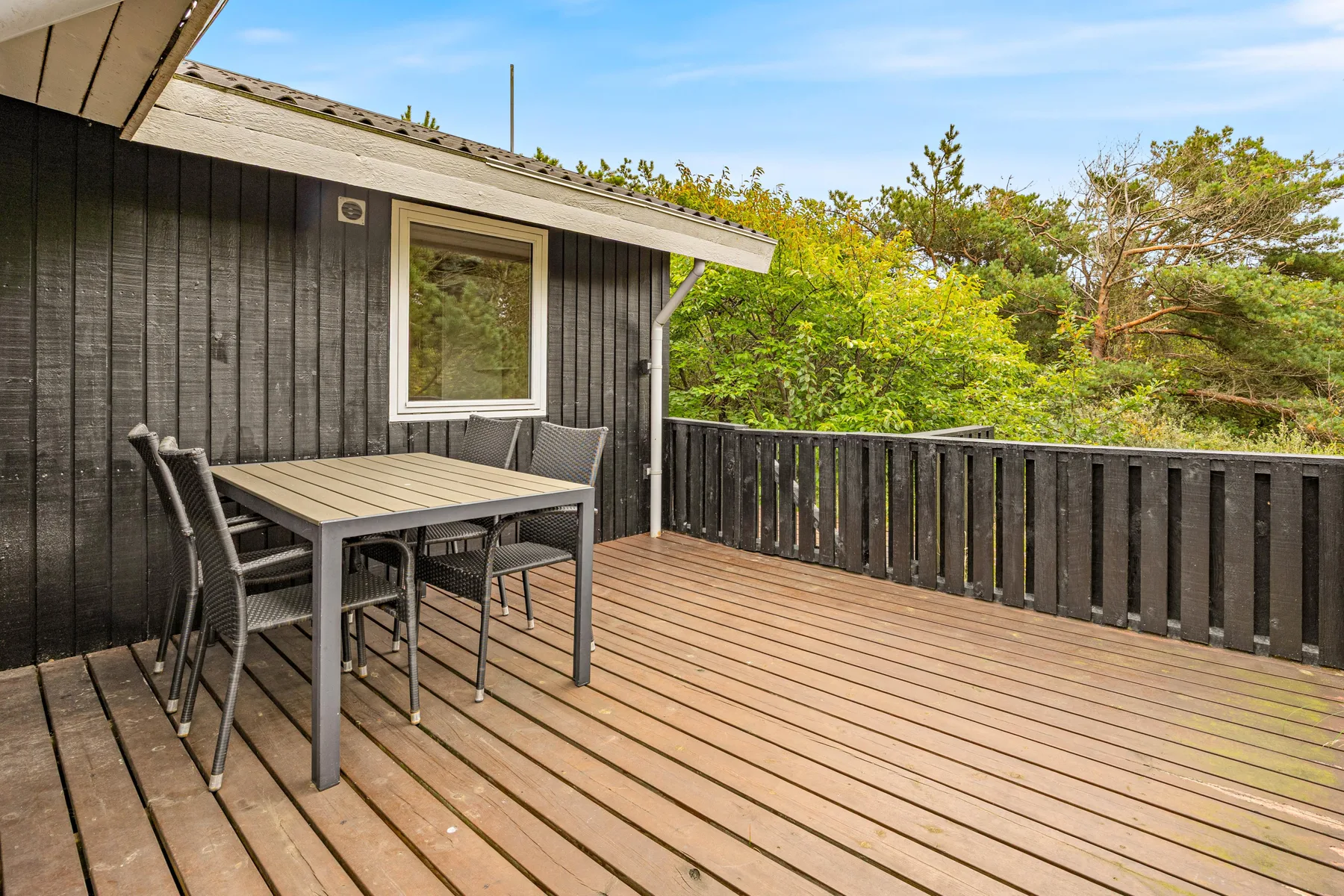 An outdoor deck with a dining table and seating beside a dark-sided house.