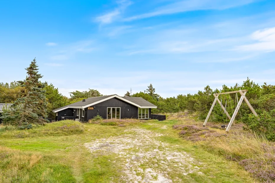 A dark house stands in a grassy clearing beside a wooden swing frame.