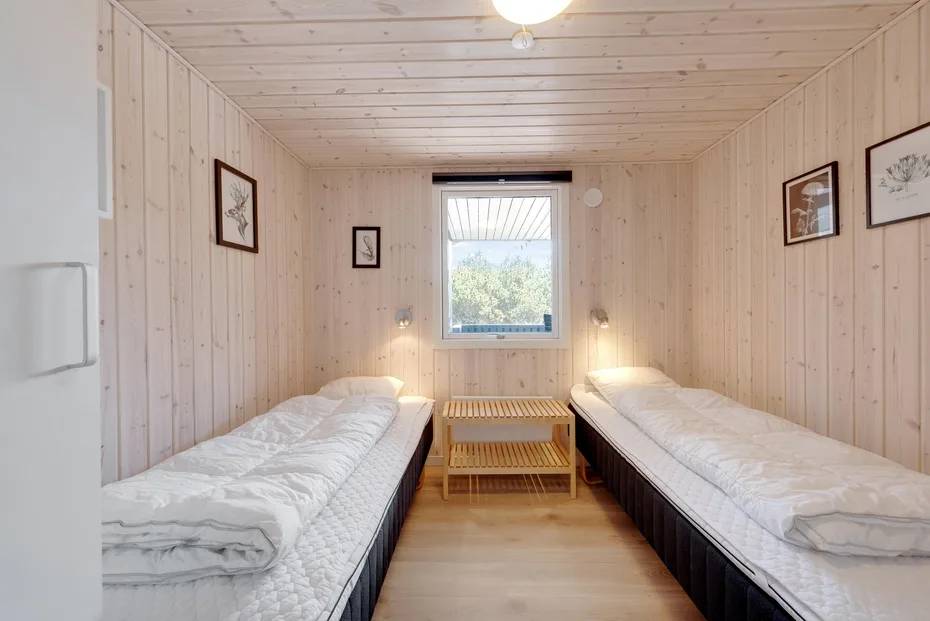 A bright bedroom has two single beds facing a small table beneath a window.
