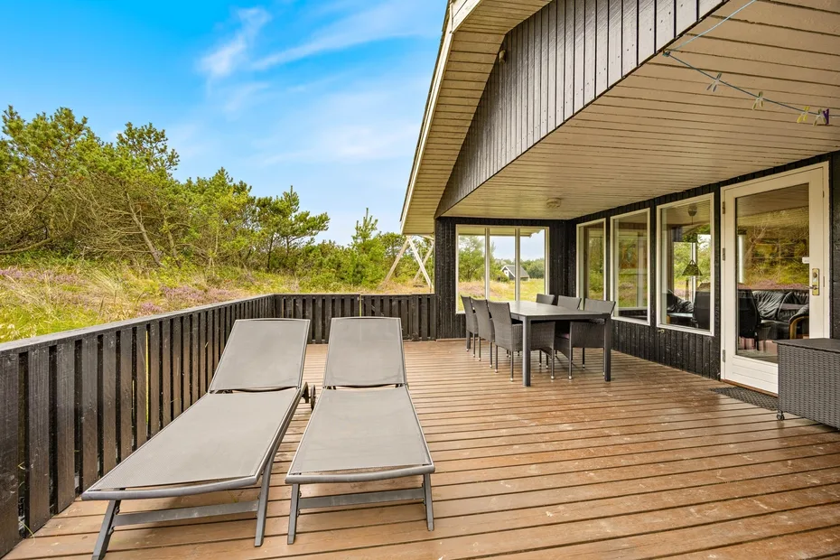 A wooden outdoor deck with lounge seating and a dining area beside the house.
