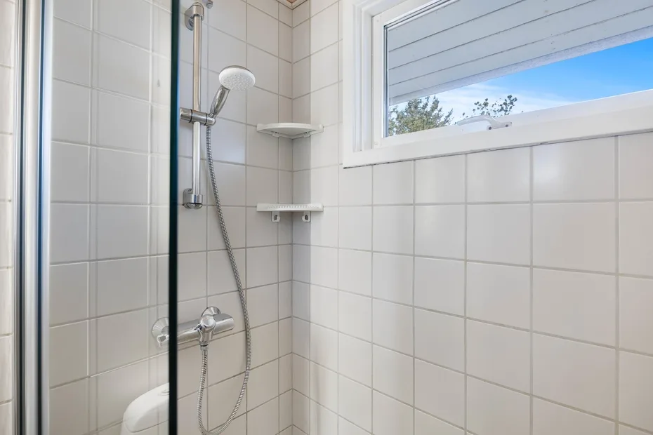A tiled shower with a handheld showerhead and a high window.