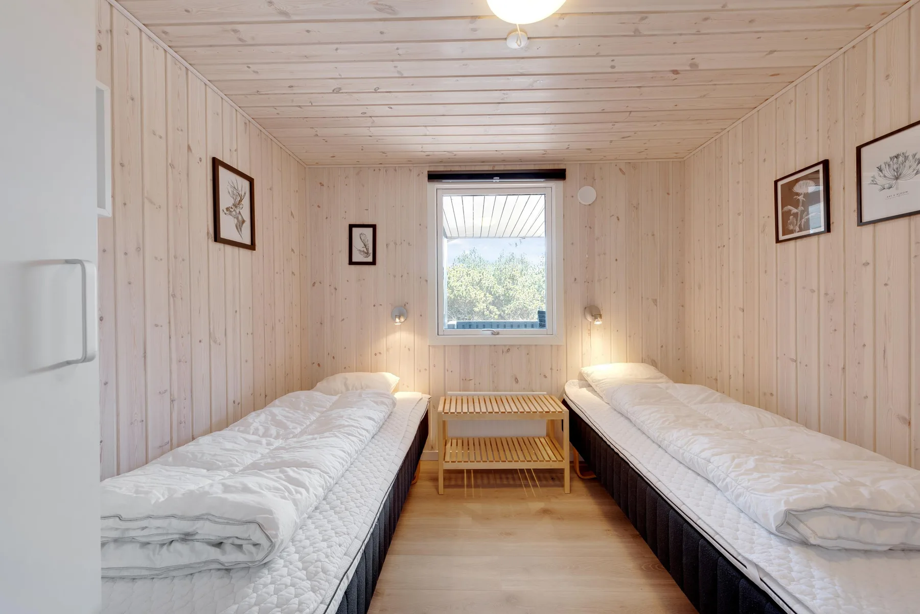 A bright bedroom with two single beds and a small table beneath the window.