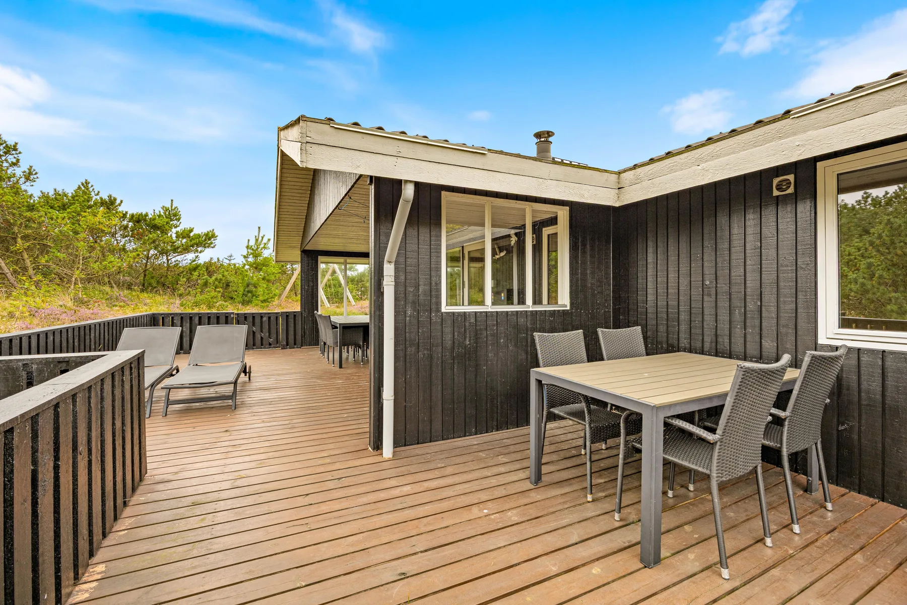 A wooden deck beside a dark house has outdoor seating and a dining table.