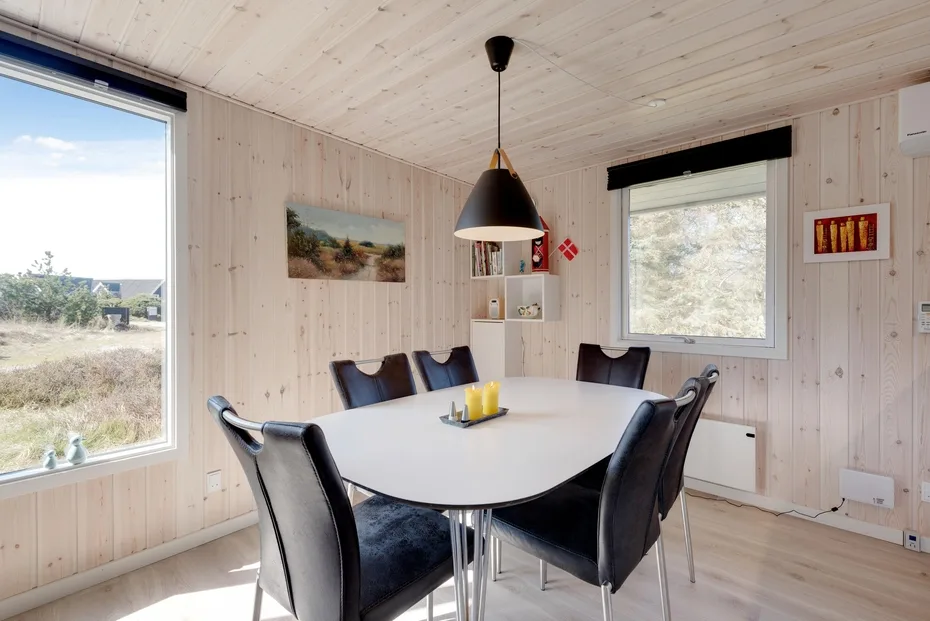 A bright dining area with a white table, dark seating, and large windows.