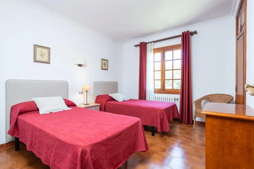 A bedroom with two beds, red bedspreads, and a window framed by red curtains.