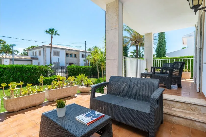 A covered outdoor patio has dark woven seating and potted plants.