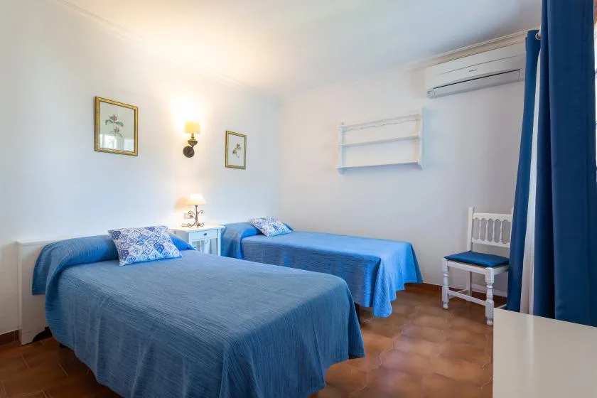 A bedroom with two beds dressed in blue covers and a blue curtain.