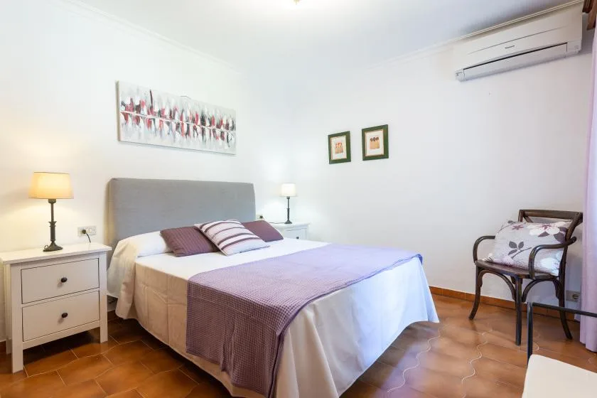 A bedroom with a neatly made bed and a chair beside it.