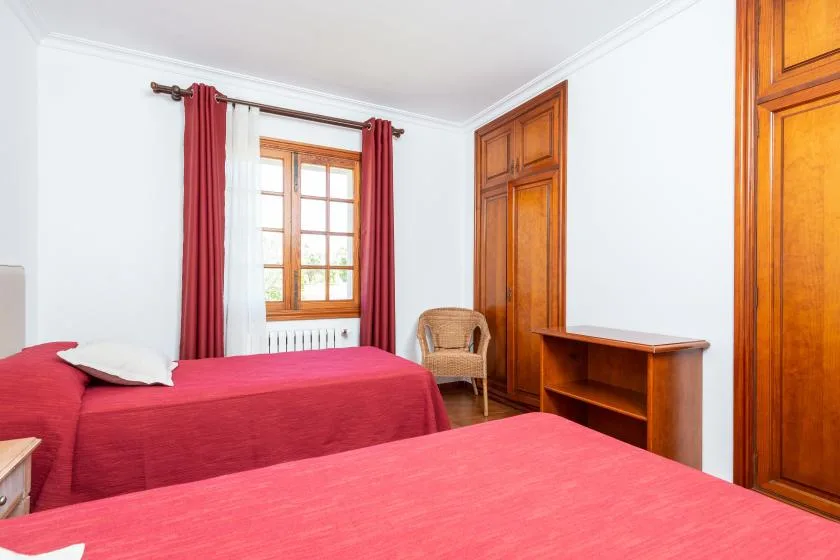 A bedroom with red-covered beds, a window, and wooden furniture.
