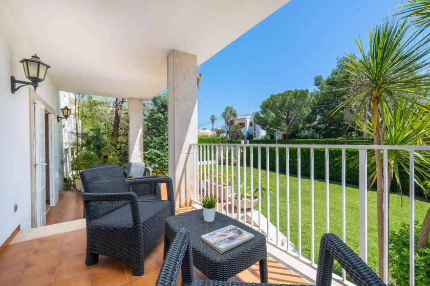 A covered outdoor terrace with seating overlooks a green lawn and trees.