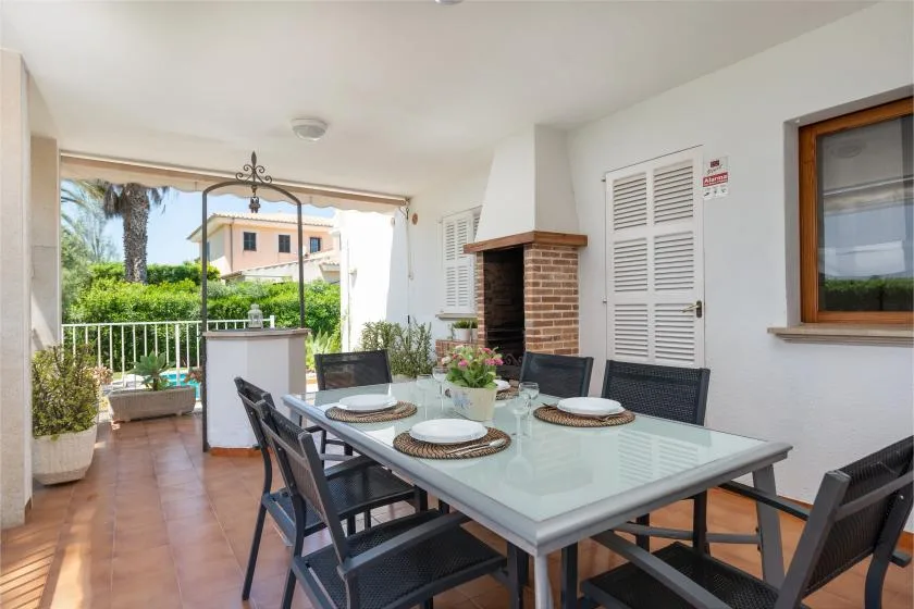 A covered patio dining area with a glass table and garden views.