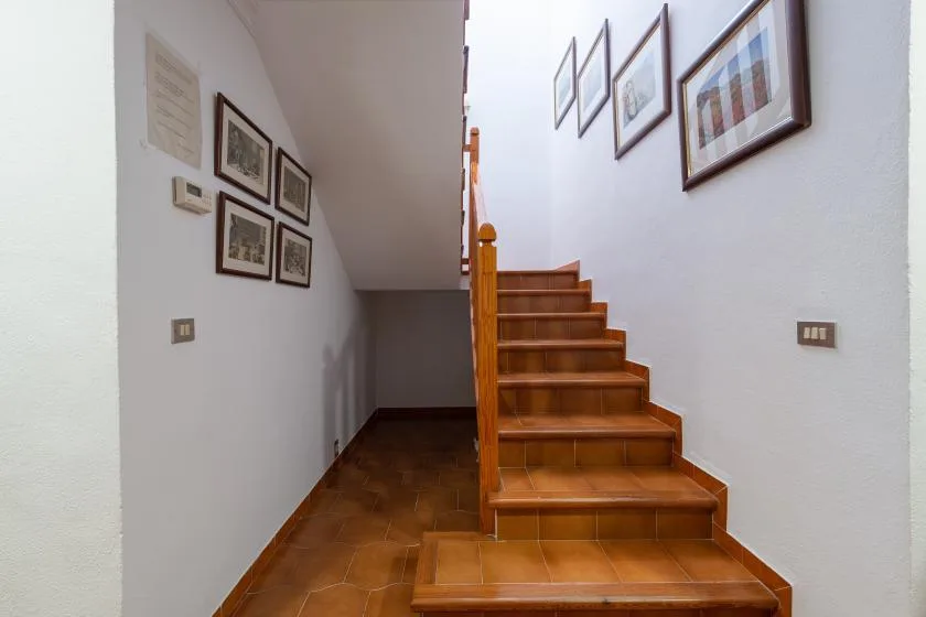 A tiled hallway with a wooden staircase and framed pictures on the walls.