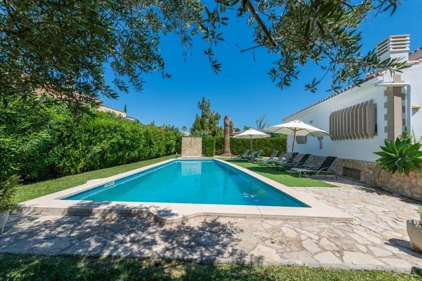 An outdoor swimming pool beside a white building, with loungers under umbrellas.
