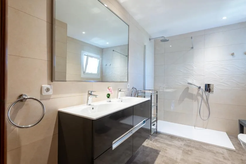 A bright bathroom with a wide vanity, mirror, and walk-in shower.
