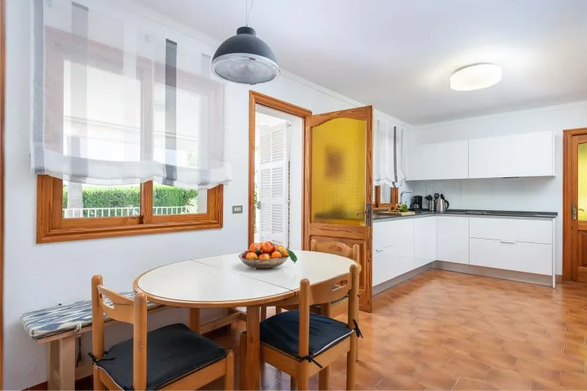 A bright kitchen with white cabinets, a dining table, and a large window.