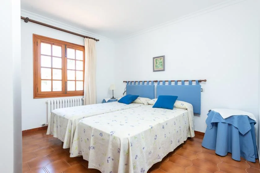 A bedroom with a double bed, blue headboard, and a wooden-framed window.