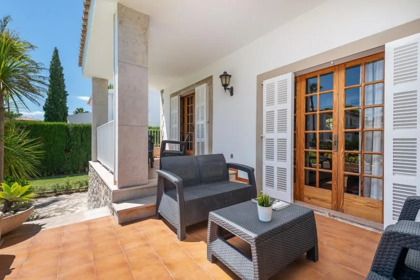 A tiled outdoor patio with seating beside glass doors and a garden.