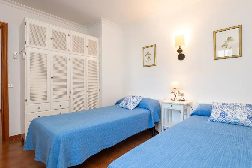 A bedroom with two beds dressed in blue linens and a small bedside table.